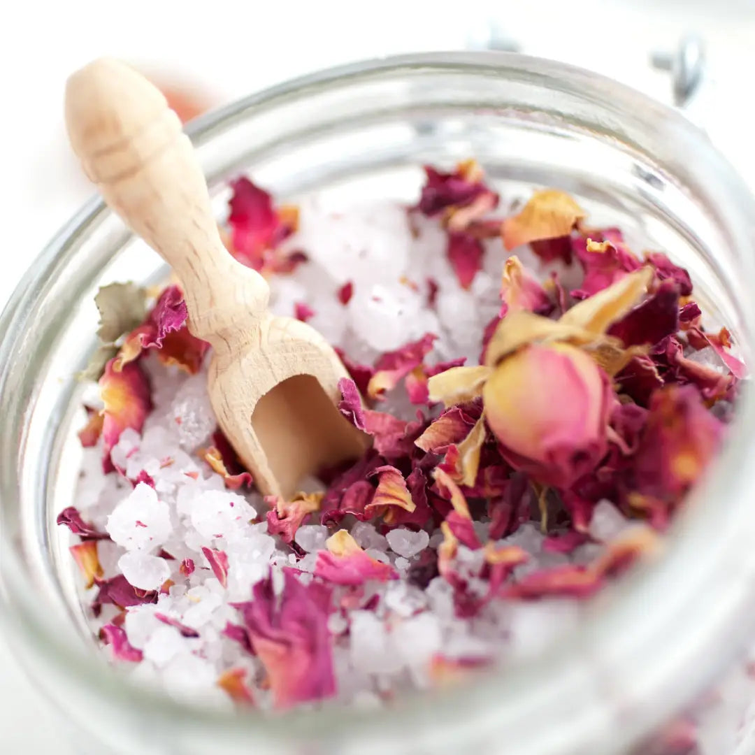 Glass jar of By Valenti English Rose Garden milk Bath Salts with pink and red roses and a wooden scoop