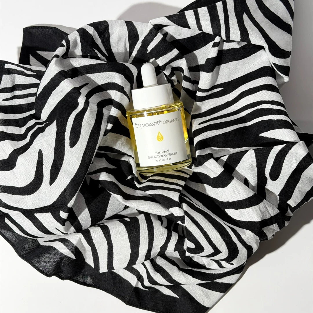 By Valenti skincare bottle of bakuchiol smoothing serum with dropper on a zebra-patterned bandana