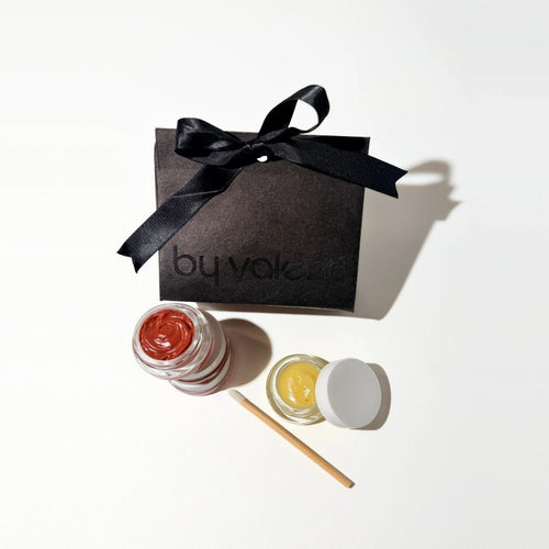 Two small jars of lip balm with a black box labeled 'by valenti' on a white background