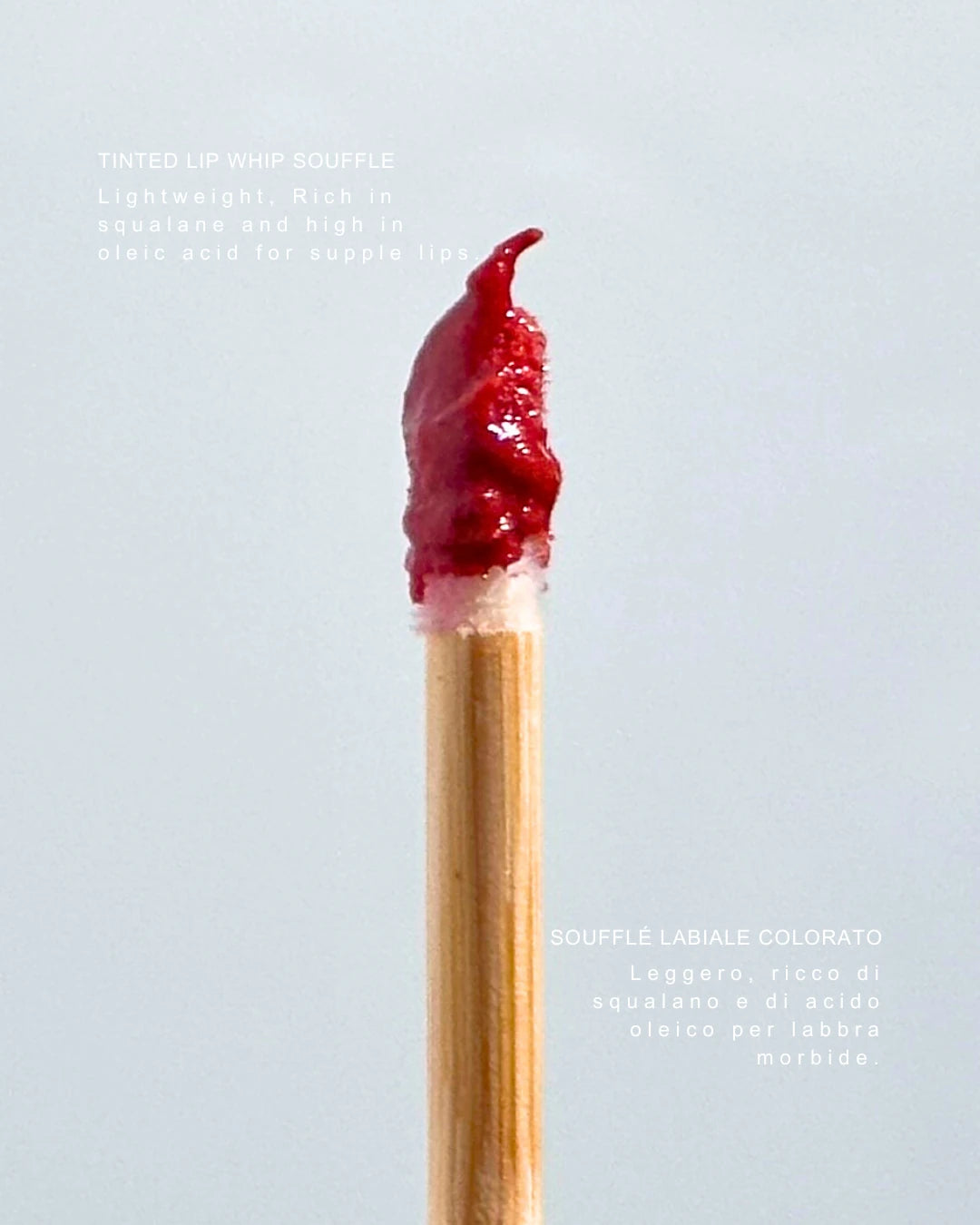 Wooden lip wand displaying By Valenti red tinted lip balm on a wooden stick against a light gray background