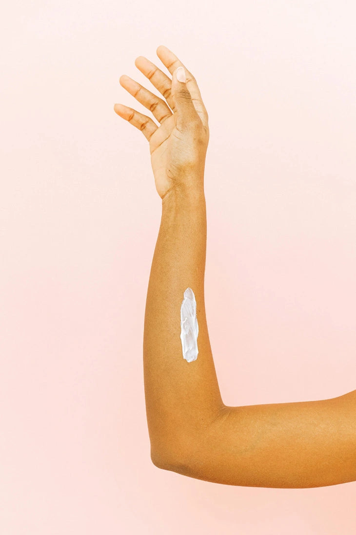 Arm of a woman with a patch of white cream on a white background