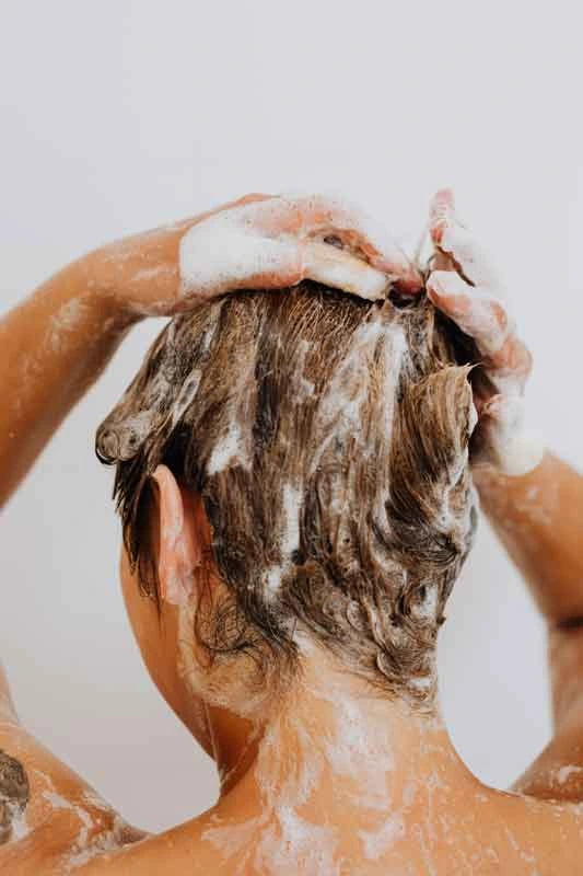Woman washing her hair with soap suds on a plain background